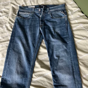 Replay Grover raka jeans blå  - Säljer ett par klassiska Replay Grover jeans i rak modell och snygg mellanblå tvätt. Jeansen har fem fickor, tydliga kontrastsömmar och läderpatch bak i midjan. Perfekta för dig som gillar en tidlös och avslappnad look.