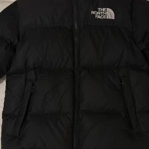 Svart dunjacka The North Face XL - Säljer en svart dunjacka från The North Face, modell 700. Jackan har en klassisk pufferstil med dragkedja framtill, två fickor och broderad logga på bröstet. Perfekt för kalla dagar och riktigt snygg till streetwear-looken.
