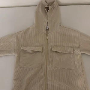 Beige ribbad hoodie från Amisu XS - Säljer en beige ribbad hoodie från Amisu i storlek XS. Tröjan har huva, dragkedja framtill och två stora fickor med lock på bröstet. Materialet är mjukt och ger en chill vibe, perfekt för lager på lager under höst och vår.