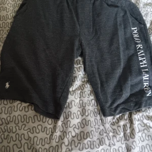 Mörkgrå shorts från Polo Ralph Lauren - Snygga mörkgrå shorts från Polo Ralph Lauren med vit logga på benet och stort tryck längs sidan. Sköna och stilrena, perfekta för chill eller träning. Mjukt material och klassisk passform.