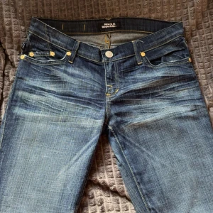 Rock & Republic blå jeans med kontrastsömmar - Snygga blå jeans från Rock & Republic med tydliga slitningar och coola kontrastsömmar i gult. Klassisk femficksmodell och dekorativa bakfickor med broderad detalj. Jeansen har normal passform och är tillverkade i jeansmaterial.