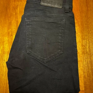 Svarta slim jeans från Tiger of Sweden - Svarta jeans från Tiger of Sweden i slim fit-modell. Klassisk femficksdesign med snygga detaljer och diskret logga på bakfickan. Tillverkade i Italien och passar perfekt för dig som gillar en stilren och modern look. Har mycket stretch så går att töja. Vid funderingar är det bara att kontakta mig jag är ärlig och rak med svar.