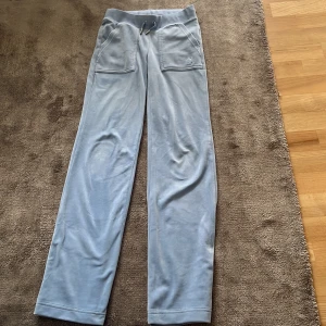 Ljusblå velourbyxor Juicy Couture XXS - Supermjuka ljusblå velourbyxor från Juicy Couture med raka ben, bred resår i midjan och snörning. Stora fickor fram och bak med snygga knappar. Perfekta för en chill och trendig look.