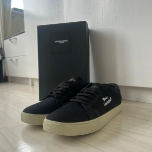 Svarta Saint Laurent sneakers - Svarta sneakers från Saint Laurent med vit broderad logga på sidan och beige sula. Skorna har snörning, rund tå. Klassisk och stilren modell med diskreta guldiga detaljer på plösen. Ps använda ca 3-6 gånger. Kvitto finns i dm, pris kan sänkas vid snabb affär 