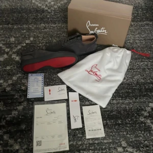 Christian Louboutin svarta sneakers - Snygga svarta sneakers från Christian Louboutin i mocka med klassisk röd sula. Lågt skaft, rund tå och snörning framtill. Kommer med originalkartong, dustbag och äkthetsbevis. Perfekta för dig som vill ha en lyxig och stilren look.