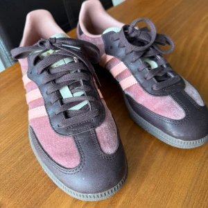 Adidas Samba i rosa sammet och brunt läder  - Snygga Adidas Samba sneakers i rosa sammettyg och brunt läder med klassiska tre ränder i ljusrosa på sidorna. Skorna har bruna snören och sula och detaljer i mörkbrunt skinn. ENDAST ANVÄNDA EN GÅNG.