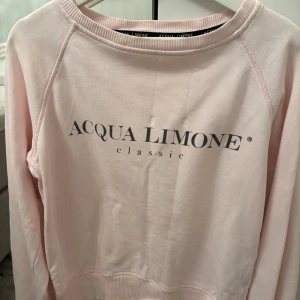  Acqua Limone sweatshirt XS - Superfin ljusrosa tjocktröja från Acqua Limone i bomull med klassisk logga framtill och stor gul citron-tryck på ryggen. Tröjan har rund hals, långa ärmar och ribbade muddar. Perfekt för dig som gillar en clean och chill stil.