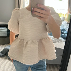 Beige blus - Supersöt beige blus med puffärmar. Baksidan har en öppen rygg med rosett som knyts i nacken. Köpt för ca 2,5 månad sedan och aldrig använd! 