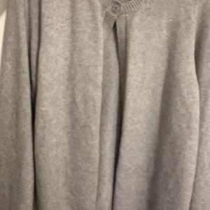 Grå stickad kofta från Gina Tricot - Mysig grå stickad tröja med lång ärm och rund halsringning med knappdetalj framtill. Enkel och stilren design som passar perfekt till jeans eller kjol. Använd fåtal gånger