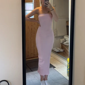 Ljusrosa bandeau midiklänning - Säljer en superfin ljusrosa, bandeau midi klänning med slim passform. Klänningen är ribbad och har en snygg slits baktill. Köptes i somras och är använd endast en gång. 