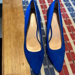 Koboltblå pumps från Misshe, stl 39 - Snygga koboltblå pumps från Misshe i storlek 39. Skorna har spetsig tå och är klädda i mockaliknande material. Perfekta för dig som vill sticka ut med färg och stil. Klassisk modell med hög klack och elegant form.