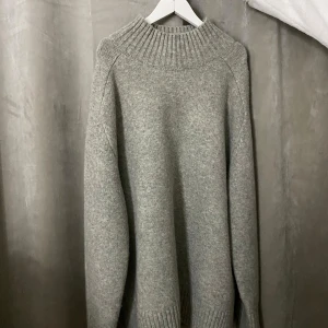 Grå stickad polotröja - Mysig grå stickad polotröja med bred ribbad krage och långa ärmar. Perfekt för kyliga dagar och enkel att matcha med jeans eller kjol. Tröjan har en loose fit och är superbekväm att bära.