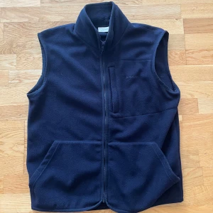 Fleeceväst från Gant - Säljer en mörkblå fleeceväst från Gant med hög krage och hel dragkedja framtill. Västen har två stora fickor och en bröstficka med diskret broderad logga. Perfekt för lager-på-lager och chillare dagar. Västen är storlek M och är true to size. Nypris: 900kr