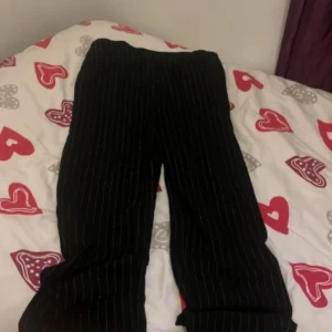 Svarta randiga kostymbyxor från Vila - Snygga svarta byxor från Vila med vita ränder. Byxorna har en elegant design och är perfekta för en stilren look. De är tillverkade i ett bekvämt material och har en elastisk midja för extra komfort. Hör av dig vid intresse (aldrig använt)