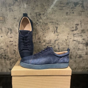 Mörkblå mockasneakers från Louboutin - Exklusiva mörkblå sneakers i mocka från Christian Louboutin med ikonisk röd sula och broderad logga på hälen. Skorna har rund tå, snörning och platt sula. Perfekta för dig som vill sticka ut med stilrena detaljer och lyxig känsla. Med kvitto och allt info om skorn.