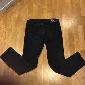 Svarta jeans från Calvin Klein - Svarta jeans från Calvin Klein. Jeansen har en diskret logga bak på linningen och är tillverkade i ett mjukt bomullsmaterial med lite stretch. Perfekta för dig som gillar stilrena och tidlösa plagg. Storlek w 31 L 32