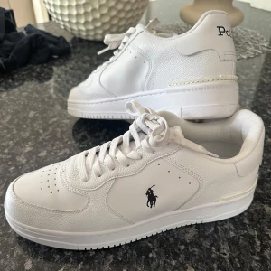 Vita sneakers från Polo Ralph Lauren - Snygga vita sneakers från Polo Ralph Lauren med logga på sidan och Polo-tryck på hälen. Skorna är tillverkade i läder med detaljer i syntet och har en platt sula samt snörning. Modell = Masters Ctr - sneakers - low top lace🤍Skorna är i väldigt bra skick, använda 1-2 gånger! NYPRIS= 1795kr