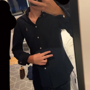 Mörkblå skjorta från Ralph Lauren S - Snygg mörkblå skjorta från Ralph Lauren i custom fit. Klassisk design med knappar hela vägen, button-down krage och ikoniska broderade loggan på bröstet. Skjortan är långärmad och gjord i mjuk bomull, perfekt till jeans eller chinos. finns en liten defekt på bild 4 men den tänker man knappt på, viker man över ärmen längs ner så blir man extar grischad och defekten synns inte! passar även xs 