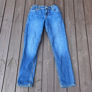 Blå jeans från Jack & Jones, stl 164 - Snygga blå jeans från Jack & Jones i klassisk modell med raka ben och normal passform. Jeansen har orangea kontrastsömmar och fem fickor. Perfekta för dig som gillar en enkel och tidlös stil.