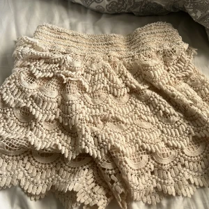 Beige virkade spets-shorts - Superfina beige shorts med detaljerad virkad spets i lager-på-lager look. De har en feminin och bohemisk vibe med snygga volanger och mönstrad spets som ger extra struktur. Perfekta för varma dagar och festivalhäng.