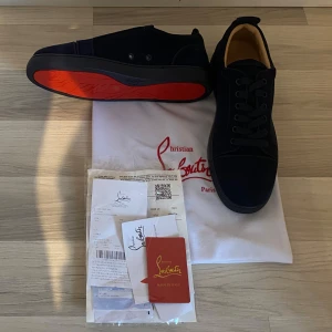 Mörkblå mocka sneakers från Louboutin - Exklusiva mörkblå sneakers från Christian Louboutin i mjuk mocka med ikonisk röd sula. Skorna har rund tå, snörning och diskret broderad logga på hälen. Insidan är i beige skinn för extra komfort. Perfekt för dig som vill sticka ut med stil.