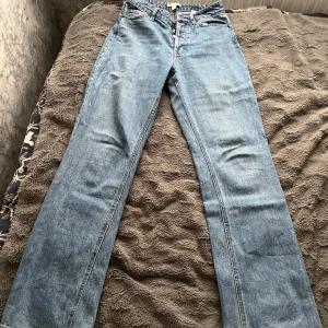 Blå raka jeans från H&M - Snygga ljusblå jeans från H&M i klassisk rak modell med fickor och silverfärgade knappar. Jeansen har normal passform, hög midja och är tillverkade i slitstarkt bomullsmaterial. Perfekta för dig som gillar en enkel och clean look. Vid frågor hör dig!