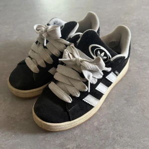 Adidas Campus svarta sneakers - Svarta Adidas Campus sneakers med klassiska vita ränder och breda vita skosnören. Dom är lite slitna, därav billigt pris!