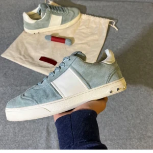 Valentino Limited Edition - Snygga Valentino sneakers i ljusblå mocka med vita detaljer och platt sula. Skorna har klassisk snörning och coola nitar på hälen. Perfekt för dig som vill sticka ut med stilrena och exklusiva sneakers. Fint Skick sparsamt använda!