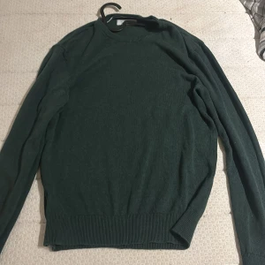 Mörkgrön tröja från Pier One - Mörkgrön långärmad tröja från Pier One med rund halsringning och ribbade muddar vid ärmslut och nederkant. Enkel och stilren design som passar perfekt till jeans eller chinos. Materialet känns mjukt och skönt mot huden.