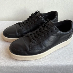 Svarta sneakers från Vagabond - Stilrena svarta sneakers från Vagabond med vit sula och klassisk snörning. Skorna är gjorda i skinn och har en rund tå samt platt sula. Perfekta för dig som gillar en clean och enkel look.