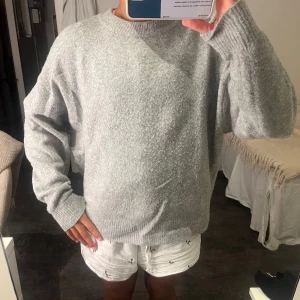 Grå stickad tröja från H&M - Mysig grå stickad tröja från H&M i storlek M. Tröjan har en rund hals, ribbade muddar och en loose passform som ger en chill vibe. Perfekt för lager-på-lager och att bara slänga på sig när det är kallt ute.