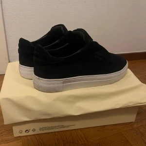 Navy blue sneakers från Axel Arigato - Stilrena navy blue sneakers från Axel Arigato i mocka med vit platt sula. Skorna har minimalistisk design utan snörning, med elastiskt band över vristen för enkel påtagning. Perfekta för dig som gillar en clean och modern look. Skorna är andvända 3 gånger 