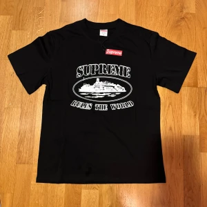 Supreme svart t-shirt med tryck - Supreme t-shirt i svart med stort vitt tryck på framsidan och handskriven text på ryggen. Klassisk Supreme box logo i rött och vitt. Rund hals och korta ärmar. Tillverkad i 100% bomull, skön och mjuk kvalitet. Perfekt för dig som gillar streetwear och statement-plagg.