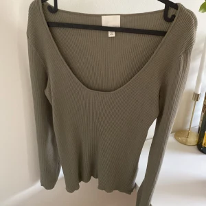 Ribbad grön långärmad tröja - Ribbad långärmad tröja i en snygg olivgrön nyans. Tröjan har en djup rundad urringning och är tillverkad i stretchigt material som sitter bra mot kroppen