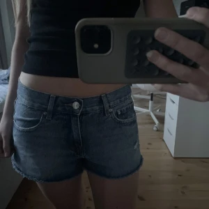 Lågmidjade jeansshorts med fransar - Snygga blå denimshorts med låg midja och fransig kant. Klassisk femficksmodell med slitna detaljer och råa benslut. Perfekta för sommaren och en avslappnad stil.