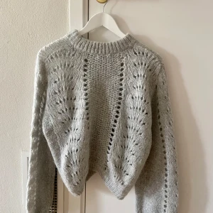 Grå stickad tröja med hålmönster - Superfin grå stickad tröja med hålmönster och bred ribbad krage. Tröjan har lång ärm och en lite loose passform. Perfekt för en sommarkväll!🌸