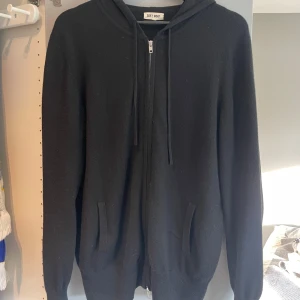 Svart hoodie i kashmir från Soft Goat - Svart hoodie från Soft Goat i kashmir. Tröjan har dragkedja framtill, huva med snörning och två fickor. Tröjan är använd med i fint skick. Skriv för fler bilder