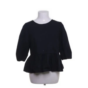 Svart blus med knyt från H&M Divided - Svart blus från H&M Divided med volang nertill och trekvartsärmar. Baksidan har öppen rygg med två snygga knytband som ger en cool detalj. Perfekt för dig som gillar en enkel men ändå trendig look.