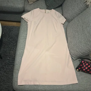 Ljusrosa klänning Holly & Whyte L - Enkel och stilren ljusrosa klänning från Holly & Whyte by Lindex. Rak modell med korta ärmar och rund halsringning. Klänningen har en synlig dragkedja i ryggen och är knälång. Perfekt för dig som gillar minimalistisk och clean stil.