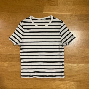 Randig ribbad t-shirt i bomull - Snygg vit t-shirt med svarta horisontella ränder och ribbad struktur. Klassisk rund halsringning och korta ärmar. Perfekt för en chill och stilren look.