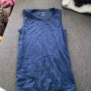 Blå linnetopp från H&M Basic - En enkel och stilren blå linnetopp från H&M Basic i mjuk ekologisk bomull. Toppen är ärmlös med rund halsringning och har en klassisk passform som funkar till allt. Perfekt för varma dagar eller som lager under en skjorta.