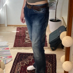 Blå vintages jeans från DENIM - Säljer blå jeans från DENIM med snyggt slitna detaljer och bruna kontrastsömmar. Jeansen har rak passform, normal midja och fem fickor. Materialet är robust bomullsdenim och färgen är mellanblå med ljusare partier. 