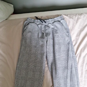 Rutiga byxor med snörning Kappahl - Snygga rutiga byxor från Kappahl i svartvitt med elastisk midja och snörning. Byxorna har raka ben och sidfickor, perfekta för en chill och stilren look. Sköna och lätta att matcha med det mesta.