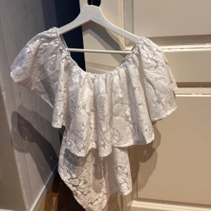 Vit spetsig offshoulder blus - Superfin vit blus i spets med bred volang och offshoulder-modell. Storlek 36 men liten i storleken!