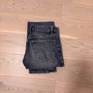  raka jeans - Säljer ett par mörkgrå jeans med klassisk femficksdesign och raka ben. Jeansen har en hög midja och är tillverkade i robust denim. Perfekta för en avslappnad och stilren look.