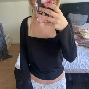 Svart långärmad topp med fyrkantig ringning - Säljer en svart långärmad topp med snygg fyrkantig ringning. Modellen är croppad och har en enkel, stilren look som passar perfekt till jeans eller kjol. Mjuk och skön i materialet, sitter tajt men ändå bekvämt.