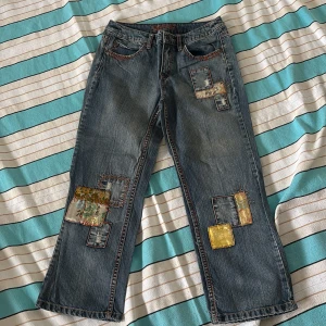 Patchade jeans från Esprit med broderi - Unika blå jeans från Esprit med färgglada patchar och broderade detaljer på både fram- och baksida. Jeansen har raka ben, orange kontrastsömmar och coola fickor med broderi. Materialet är klassisk denim och patcharna har inslag av gult och mönster. Passar för XS-S