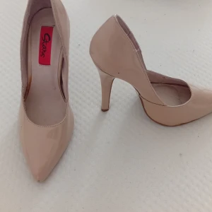 Beiga pumps med spetsig tå från Stars - Snygga beiga pumps från Stars med hög klack och spetsig tå. Skorna har en glansig finish och är tillverkade i syntetmaterial. Perfekta för dig som vill ha en clean och elegant look med extra höjd.