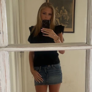 Volang topp - Supersöt svart blus från Holly White med volangärmar och fina spetsdetaljer längs kanterna. Blusen har rund halsringning.