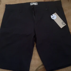 Svarta shorts från Solid - Stilrena svarta shorts från Solid med klassisk passform. De har fickor fram och bak, bälteshällor och stängs med knapp och dragkedja. Perfekta för sommardagar och enkla att matcha med det mesta. Materialet känns mjukt och svalt.
